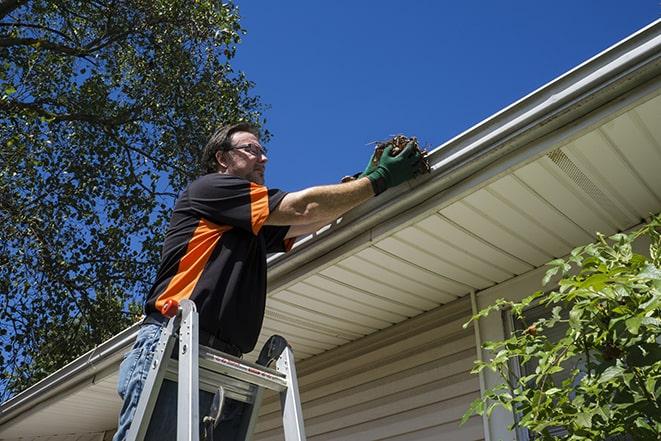 a worker on a rooftop repairing gutters and downspouts in Canadian Lakes MI